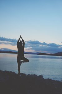 Rear view of woman doing yoga on shore at beach during sunset