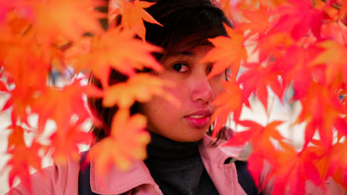 Portrait of young woman wearing hooded jacket seen through maple leaves