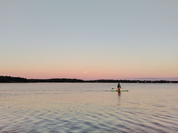 Silhouette man standing in sea against clear sky during sunset