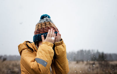 Young boy with covering his face with his hands whilst playing in snow