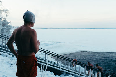 Man standing on railing by sea against sky
