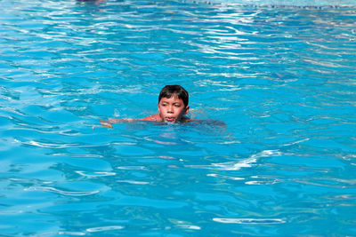 High angle view of boy looking away while swimming in pool during sunny day