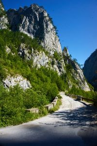 Road amidst trees and mountains against clear blue sky