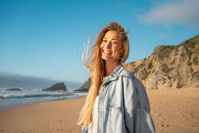 Young woman standing at beach against sky