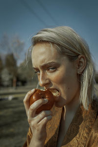 Portrait of woman eating apple against clear sky