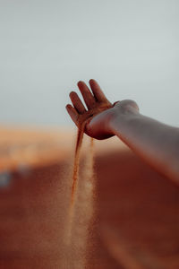 Close-up of woman hand holding sand against sky