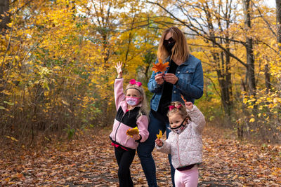 Portrait of girls with mother wearing mask standing in forest during autumn