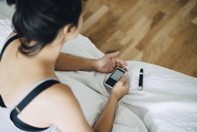 High angle view of woman checking blood sugar level while sitting on bed