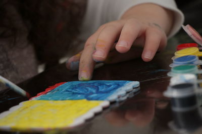 Cropped hand of girl painting tile on table
