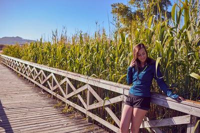 Young woman standing on footbridge by railing at field during sunny day