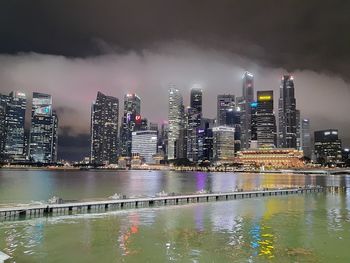 Illuminated buildings by river against sky at night