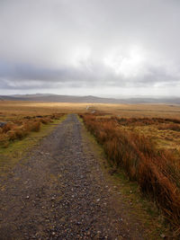 Dirt road amidst field against sky