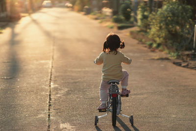 Rear view of boy riding bicycle on street