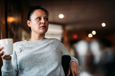 Adult woman sitting in restaurant holding coffee looking off into the distance.