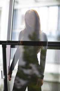 Thoughtful young woman standing by windows