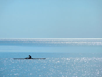 Silhouette person in boat at sea against clear blue sky on sunny day