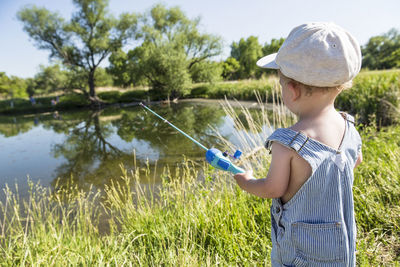 Rear view of boy wearing bib overalls while fishing in lake at park