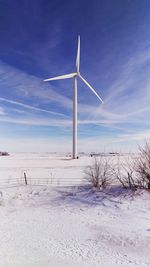 Wind turbine on snow covered field against sky during winter