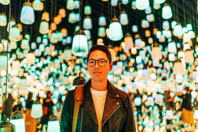 Young man looking away while standing against illuminated lights