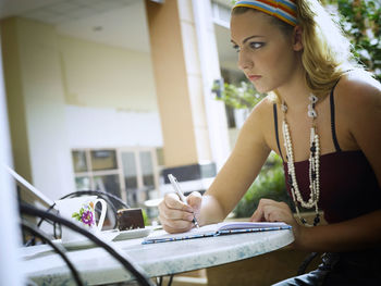 Young woman writing in diary while sitting at table