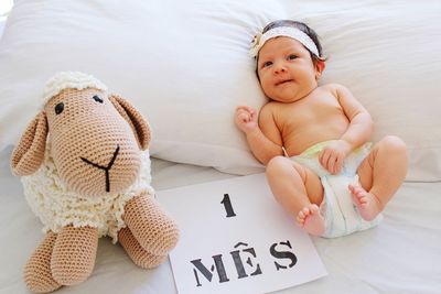 High angle portrait of cute baby girl relaxing by stuffed toy on bed