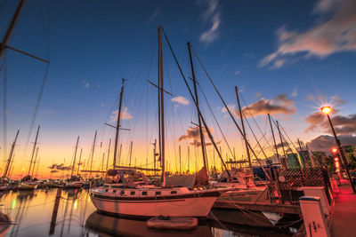 Sailboats moored on sea against cloudy sky during sunset