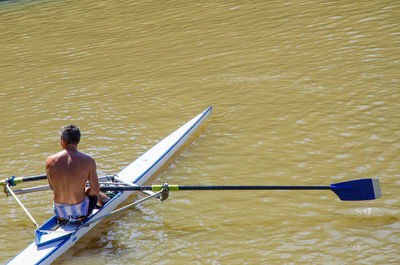 Shirtless man rowing boat on river