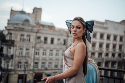 Portrait of young woman standing against building in city