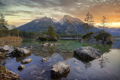 Rocks by lake against sky during sunset