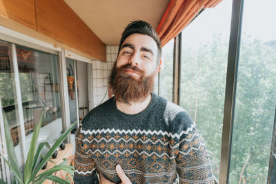 Portrait of young man standing against window