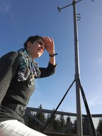 Low angle view of woman shielding eyes while standing by weather vane