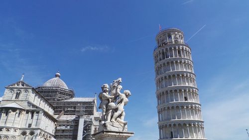 Low angle view of statues by piazza dei miracoli and leaning tower of pisa against sky