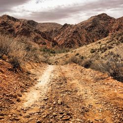 Dirt road leading towards mountains against sky
