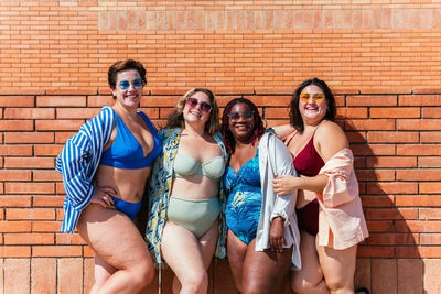 Portrait of smiling friends standing against brick wall