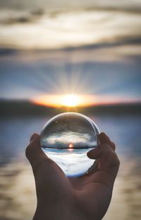 Midsection of person holding crystal ball at sunset