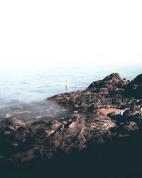 Man standing on rock by sea against sky