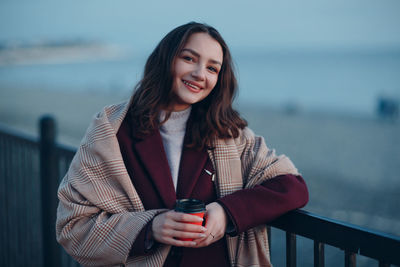 Portrait of smiling young woman standing against railing