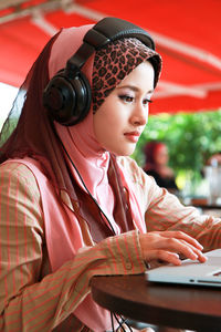 Woman wearing hijab while using laptop at outdoor cafe