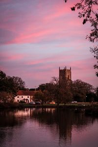 Buildings by lake against sky at sunset
