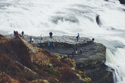 High angle view of people standing on cliff by waterfall at gullfoss iceland