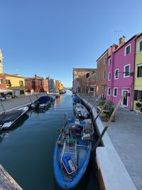 Boats moored in canal by buildings against blue sky