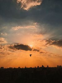 Silhouette airplane flying over city against sky during sunset