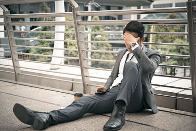 Depressed businessman sitting against railing in city