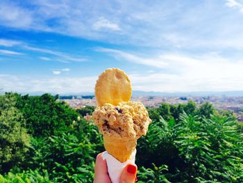 Close-up of hand holding ice cream cone against trees