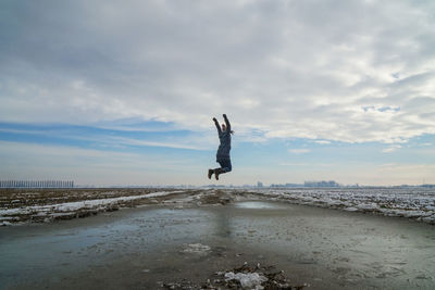 Woman with arms raised jumping at beach