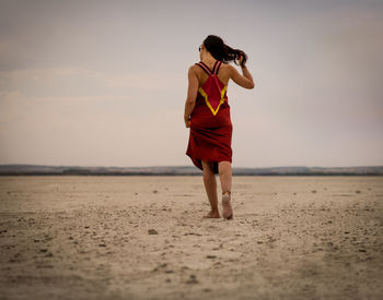 Full length of woman standing on beach viewed from behind with low angle