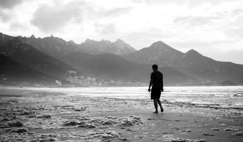 Rear view of silhouette man standing at beach against sky