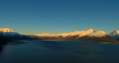 Scenic view of snowcapped mountains by sea against clear sky