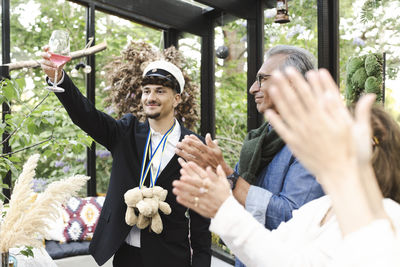 Young man raising toast while standing with family applauding during party