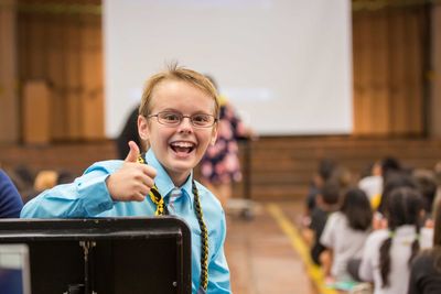 Portrait of smiling boy gesturing thumbs up sign while sitting in school